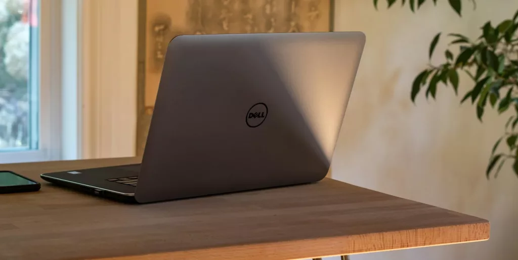 A Dell Laptop On A Table with a Curtains & Window As Background