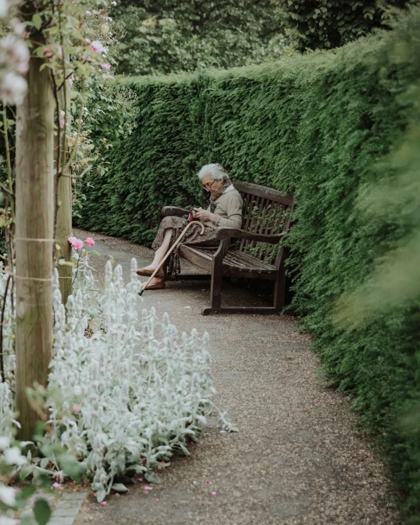 An Old Lady Sitting On Bench in woods.