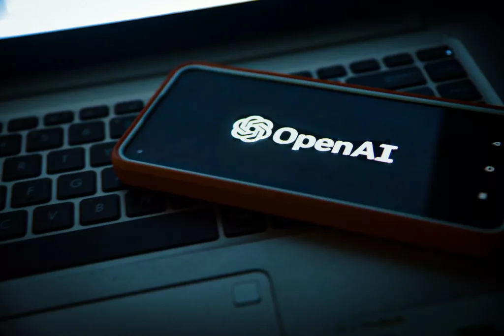 A Phone Screen on laptop keyboard Displaying OpenAI Logo Text