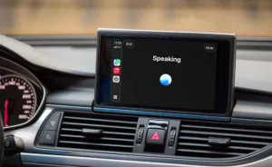 Car dashboard display showing a voice assistant interface labeled “Speaking,” with a glowing blue orb in the center and a vertical row of app icons on the left side of the screen.