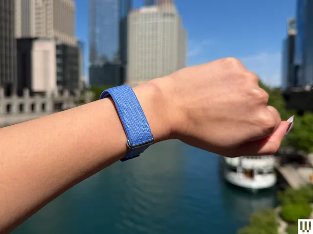 Best Fitness Trackers 2026: Top 3 Picks from Garmin, Oura & Fitbit A person's wrist wearing a blue band with a city skyline and river in the background