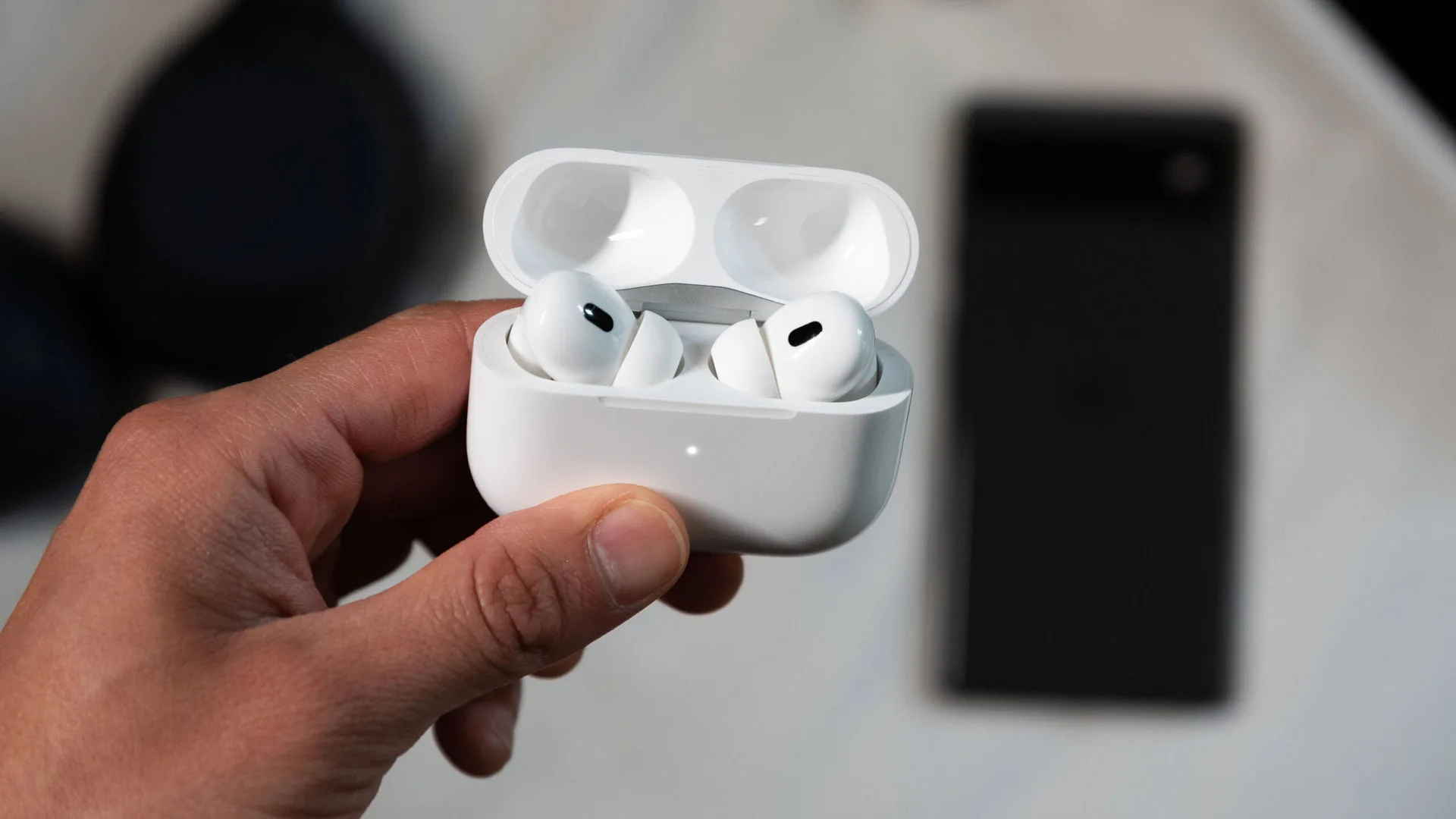Apple Camera AirPods: New 2027 Launch Window Confirmed Apple camera AirPods — A hand holds the AirPods Pro 2nd generation while in pairing mode in front of a Pixel 6 phone.