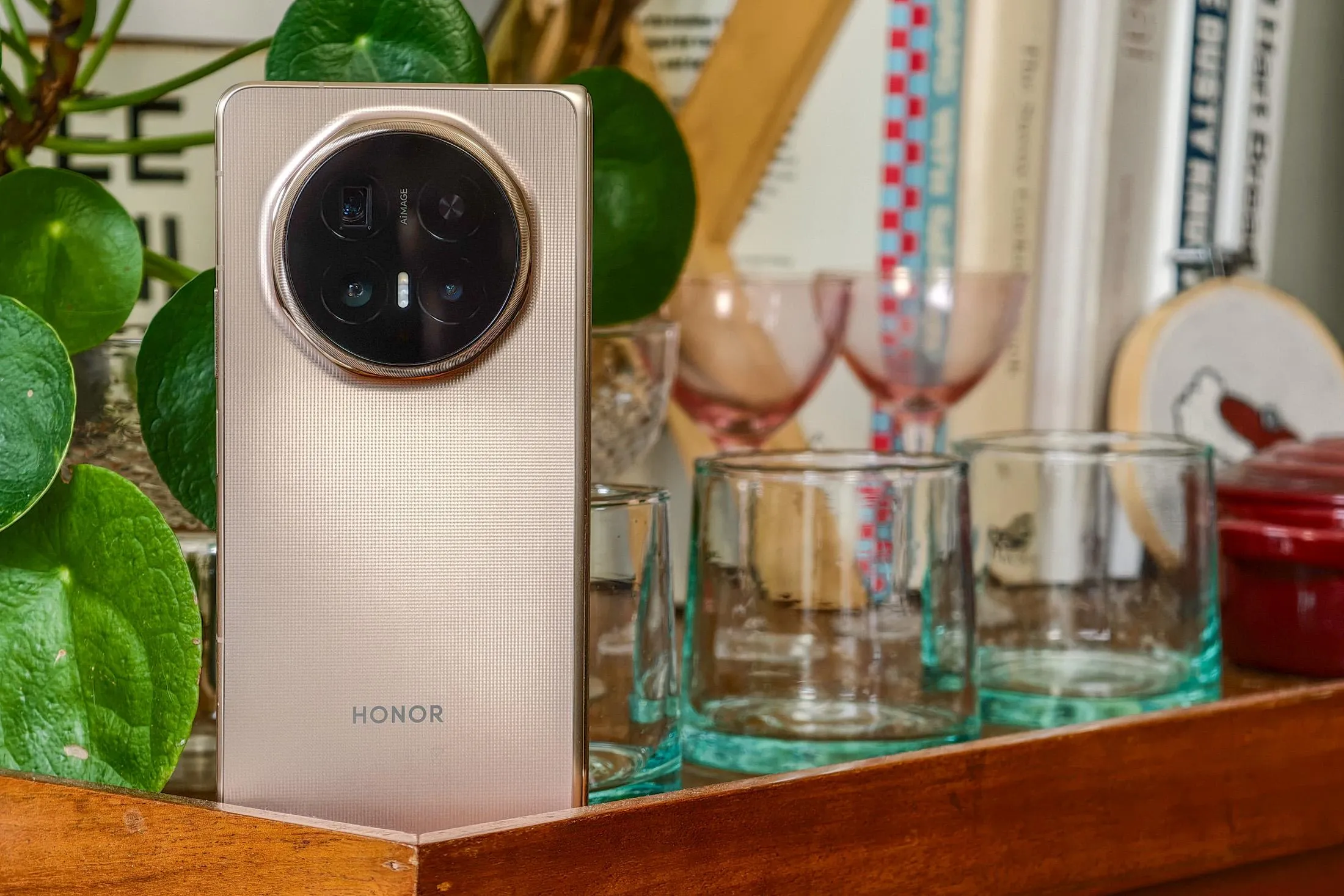 Honor Magic V6 Review: 3 Foldable Firsts, 1 That Actually Matters Photo of Honor Magic V6 on a wooden trolley with a pot plant and glassware, closed and showing the rear