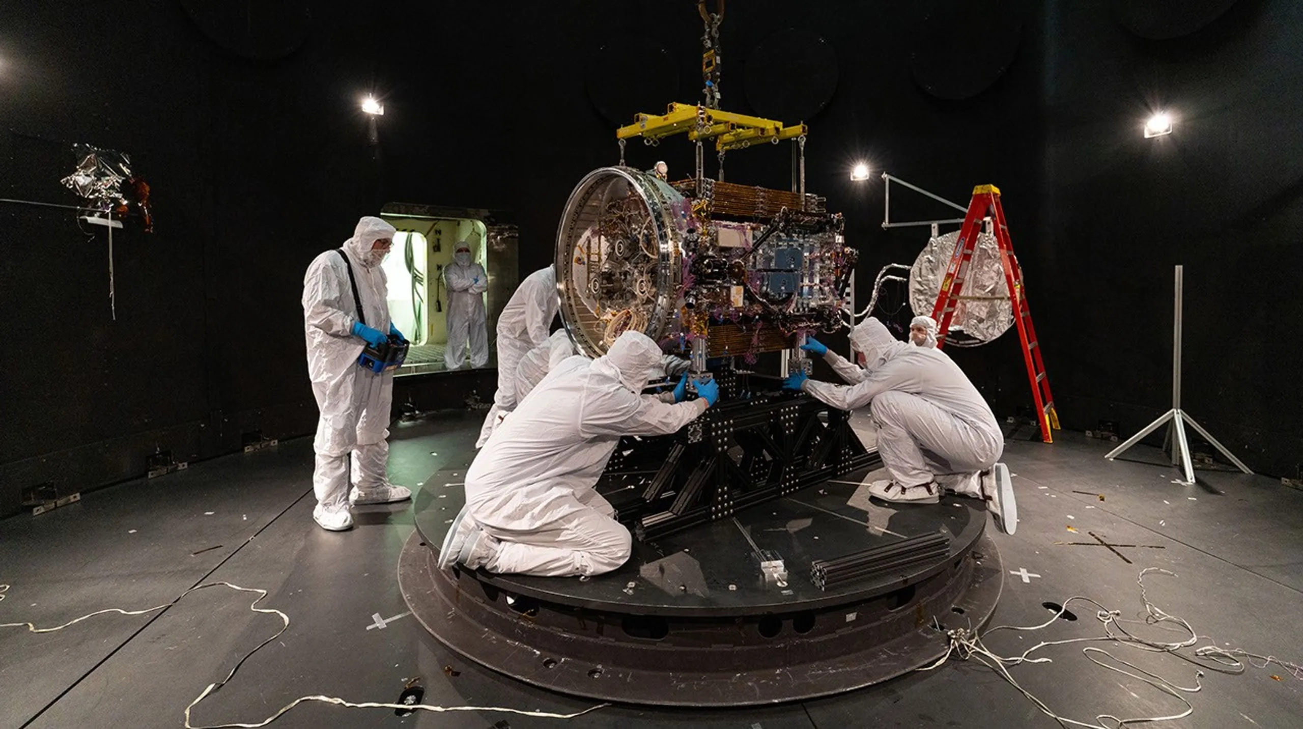Swift Boost Mission: NASA's 20-Year-Old Telescope Gets a Second Life People in clean suits work on a spacecraft in a large chamber.