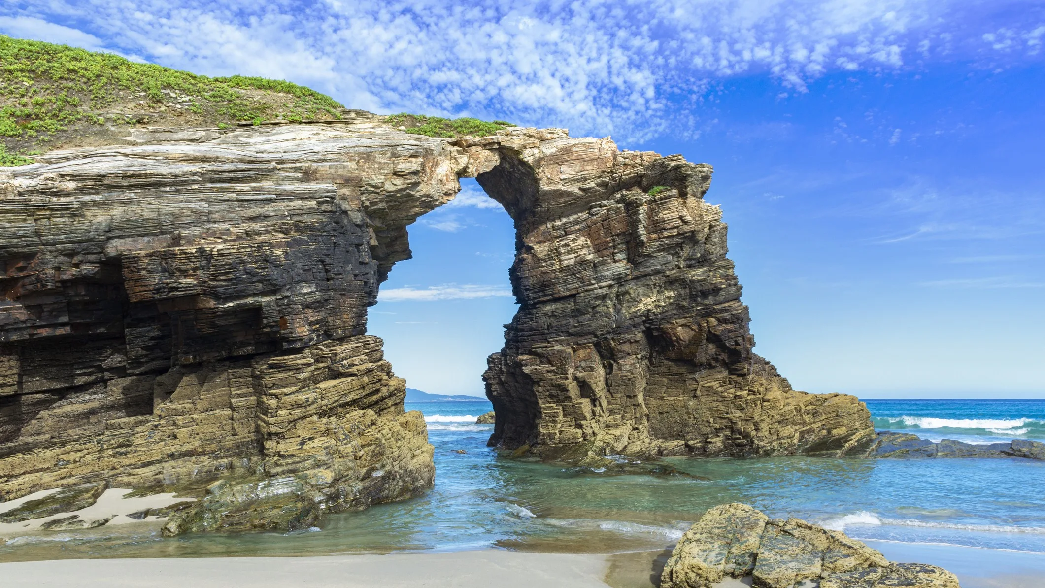 Best Spanish Beaches for the 2026 Total Solar Eclipse: 10 Top Picks impressive looking rock structure in the shape of an arch. deep blue sky above and light blue waters below.