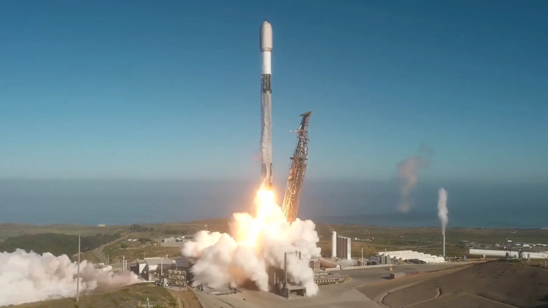 SpaceX Starlink Hits 10,600 Satellites Days Before Major IPO A white, black and gray rocket lifts off into a blue sky from an oceanfront launch pad.
