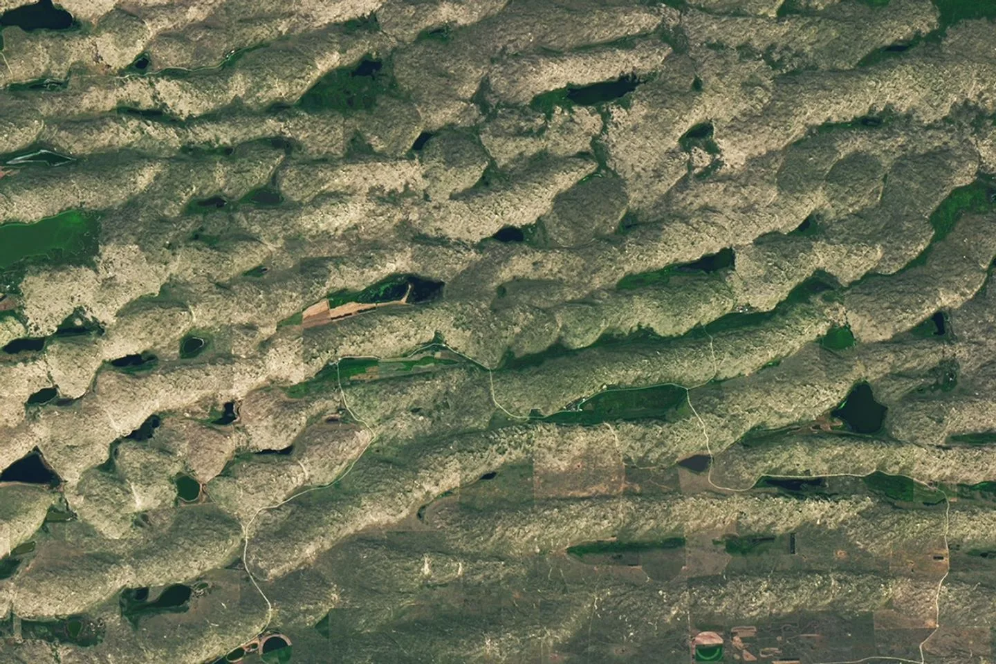 NASA Satellite Puzzler June 2026: Can You Crack It? NASA satellite puzzler — A series of tan parallel ridges runs from left to right, with green areas and small lakes filli