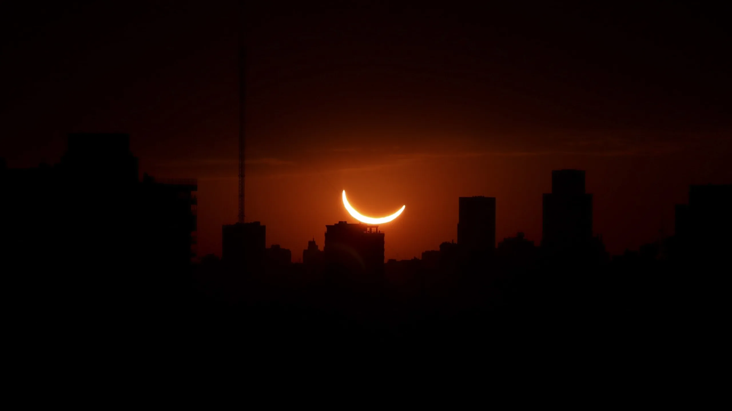 2026 Solar Eclipse: Best Places to See a Partial Eclipsed Sunset 2026 solar eclipse — the sun appears as a thin crescent and glows a deep orange hue above silhouetted buildings it is lo