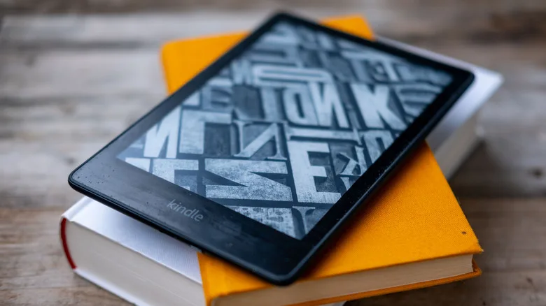 Free Kindle Books: The Best Sources You're Not Using Yet free Kindle books — A kindle sits atop a stack of hardcover books atop of a wooden table.