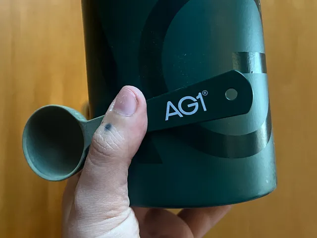 Best Greens Powders 2026: Top 16 Picks, Expert-Tested best greens powders — A hand holding up a dark green container of Athletic Greens AG1 and a small scoop