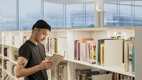 Finland's Libraries Are Proving Books Were Never the Point Finnish public libraries — Oodi Library, Helsinki Person with a black beanie and a black t-shirt reads a book while stan