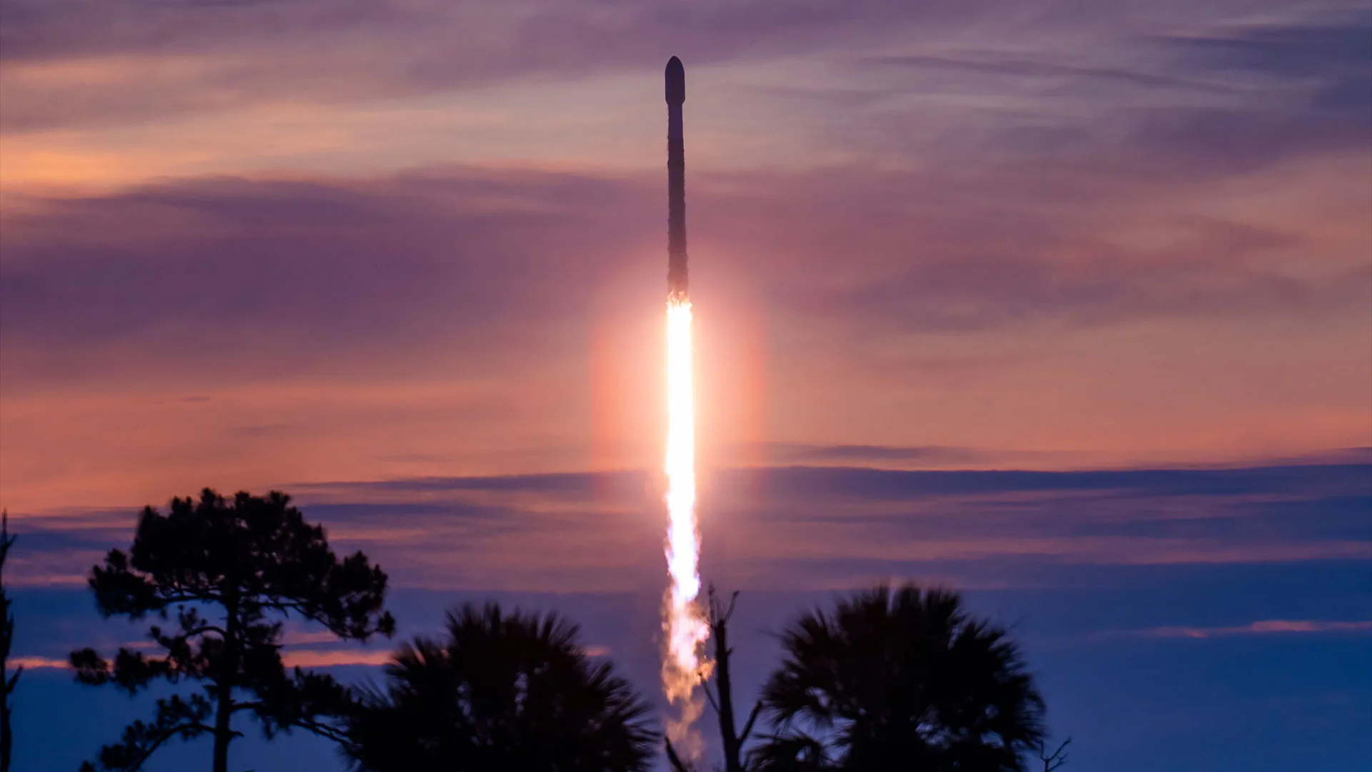 Falcon 9 Booster 1067 Sets New SpaceX Record with 36th Launch Falcon 9 record launch — A rocket lifts off into the dawn sky, set against purple clouds and a pinkish-orange horizon