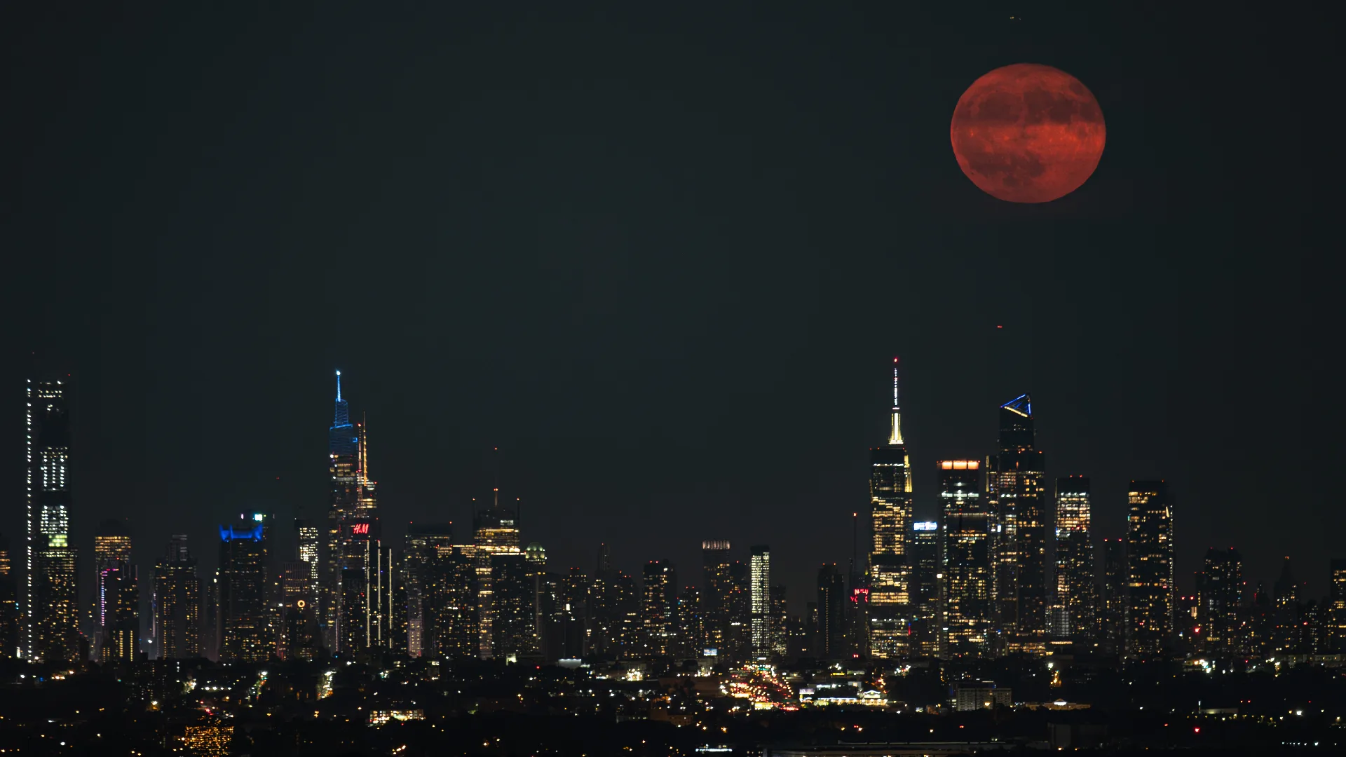 July 2026 Buck Moon: Your Complete Guide to Seeing It July full moon 2026 — A red full moon rises in a dark sky above a city skyline crowned by skyscrapers.