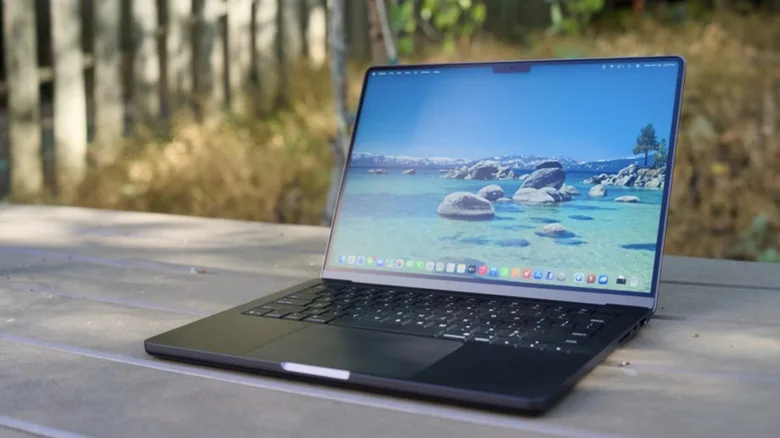 Apple MacBook Pro Redesign Is Coming — Here's the Latest MacBook Pro redesign — Photo of a 2025 entry-level MacBook Pro showing a default home screen of rocks in beachside shall