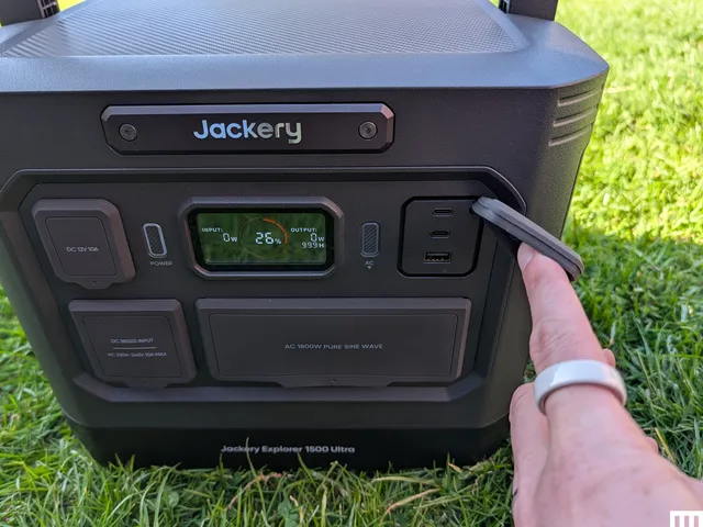 Best Portable Power Stations of 2026: Top 9 Tested Closeup of a black portable power station showing a small screen and a hand holding back the cover of an outlet