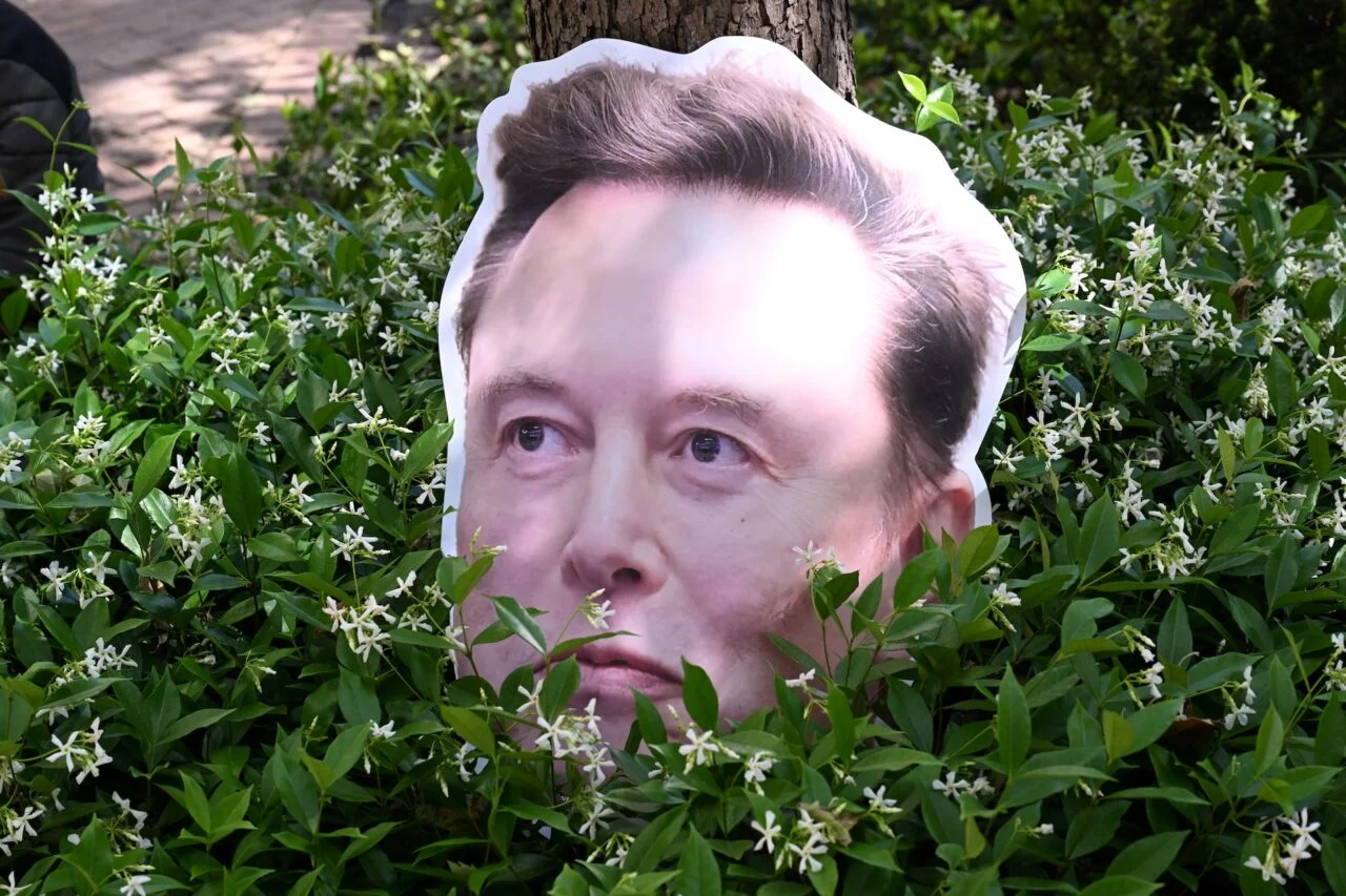 SpaceX IPO Claims Collide With the Facts on Musk’s AI Plans An Elon Musk sign sits in a bush the federal courthouse during proceedings in the trial over Elon Musk's lawsuit ag