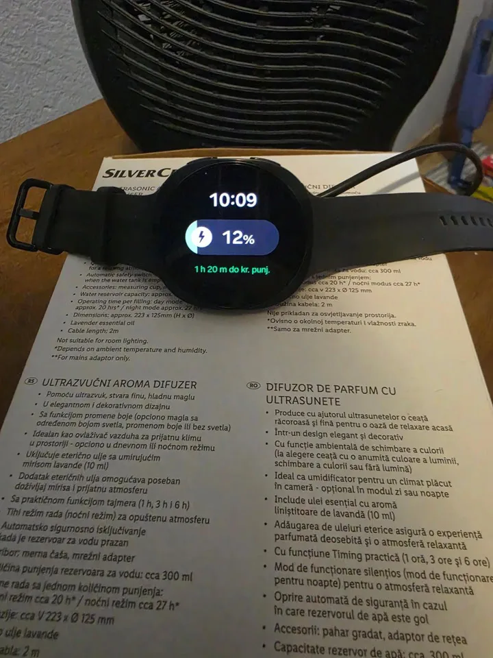 Galaxy Watch 9 charging has a critical heat problem Black Samsung Galaxy Watch 9 resting in front of a desk fan showing 12 percent battery charge at 10:09 AM at the start o